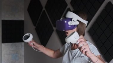 VR kasklı genç bir kadın evde oyun oynuyor. Sanal gerçeklik fütüristik kulaklık kullanan duygusal kadın ve kontrolörler üç boyutlu bir oyun oynuyorlar. Modern eğlenceyi harcamak. Meta-evrene daldırma.