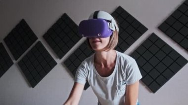 VR kasklı genç bir kadın evde oyun oynuyor. Sanal gerçeklik fütüristik kulaklık kullanan duygusal kadın ve kontrolörler üç boyutlu bir oyun oynuyorlar. Modern eğlenceyi harcamak. Meta-evrene daldırma.