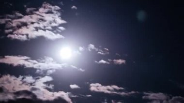 Full moon moves in the night sky through dark clouds, Timelapse. The mystical bright moon rises up against the background of clouds. Moonlight shines in the black night sky. Time lapse. 4K