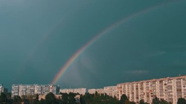 Bright rainbow in the sky over the city. Big double colorful rainbow over houses. Strong rainbow above the city skyline over the houses and buildings in the daytime. The vivid phenomenon of nature. 4K