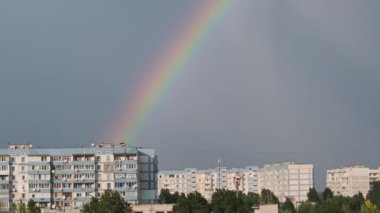 Bright rainbow in the sky over the city. Big colorful rainbow over houses. Strong rainbow above the city skyline over the houses and buildings in the daytime. The vivid phenomenon of nature. 4K