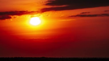 Timelapse of Dramatic sunset with sun rays in the sky through orange layered clouds. The big bright orange sun with sun rays moves down over the horizon. Awesome epic cloud space. Time Lapse. Sundown