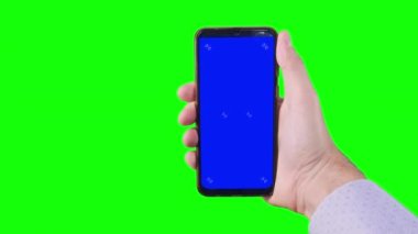 Male hand holding a smartphone with a blue screen and trackers on a green background. Chroma key. Alpha channel. Using the Device. Mobile Phone Screen. Replace blue screen and green screen. 4K