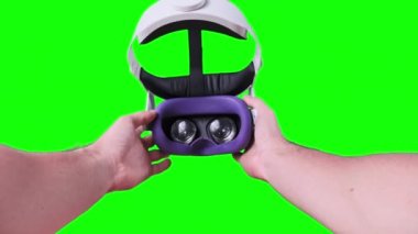 Point of view young man putting on VR Headset on green screen. POV of taking on VR glasses virtual reality. Young male hands hold virtual reality helmet. Close-up. Using VR Mask. Alpha channel, 4K