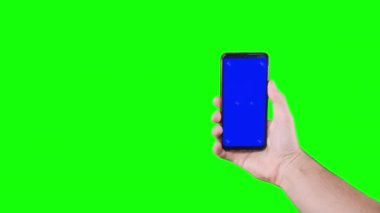 Male hand holding a smartphone with a blue screen and trackers on a green background. Chroma key. Alpha channel. Using the Device. Mobile Phone Screen. Replace blue screen and green screen. 4K