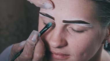 Building the shape of the eyebrows. Beauty salon. Eyebrow master dyes them for a young woman. Eyebrow correction and tint procedure. Girl sits with natural brown henna on brows. Close-up face. 4K