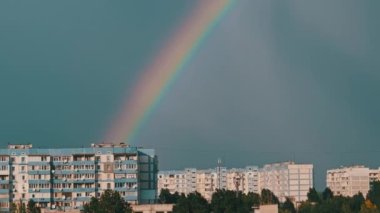 Bright rainbow in the sky over the city. Big colorful rainbow over houses. Strong rainbow above the city skyline over the houses and buildings in the daytime. The vivid phenomenon of nature. 4K