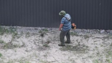 Adam yavaş çekimde çimleri manuel benzin çim biçme makinesiyle biçiyor. Çim biçme makinesiyle çim biçme işlemi. Kamu çalışanının en üst manzarası yeşil çimleri biçiyor. Bahçe bakımı aletleri. Yaz.