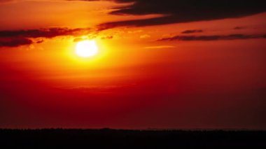 Timelapse of Dramatic sunset with sun rays in the sky through orange layered clouds. The big bright orange sun with sun rays moves down over the horizon. Awesome epic cloud space. Time Lapse. Sundown