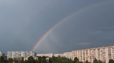 Bright rainbow in the sky over the city. Big double colorful rainbow over houses. Strong rainbow above the city skyline over the houses and buildings in the daytime. The vivid phenomenon of nature. 4K
