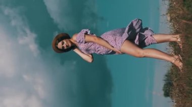 Dikey, açık tenli, mor elbiseli, hasır şapkalı, yeşil çayırda yürüyen, kıvrılan, ağır çekimde güzel bir kadın. Gökyüzüne karşı gülümseyen ve kameraya bakan çekici bir kızın portresi. Yaz yaşam tarzı