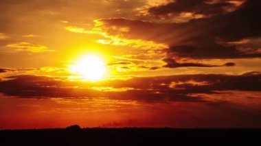 Dramatic sunset with sun rays in the Sky through orange layered clouds, Timelapse. The big bright orange sun with sun rays moves down over the horizon. Awesome epic cloud space. Time Lapse. Sundown