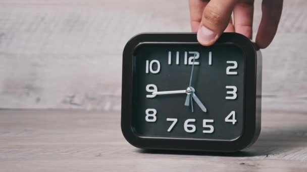 男性の手は木製のテーブルの上に矢印機械式時計を置きます 正方形の形のポインタ茶色の時計は時間を示しています 秒針が丸い文字盤のクローズアップに沿って動きます コンセプトスケジュール 早起き 毎日のルーチン — ストック動画