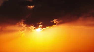 Dramatic sunset with sun rays in the Sky through orange layered clouds, Timelapse. The big bright orange sun with sun rays moves down over the horizon. Awesome epic cloud space. Time Lapse. Sundown