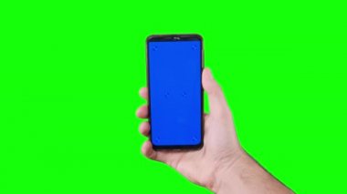 Male hand holding a smartphone with a blue screen and trackers on a green background. Chroma key. Alpha channel. Using the Device. Mobile Phone Screen. Replace blue screen and green screen. 4K