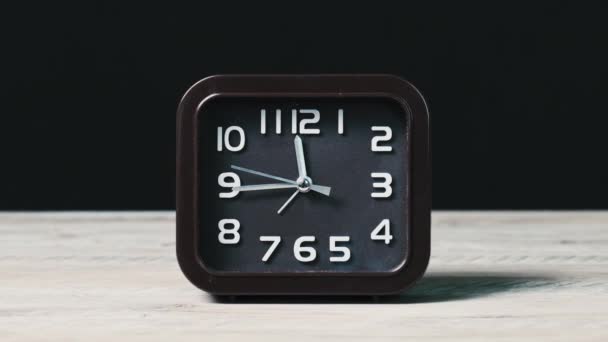木製のテーブルと黒の背景ショーの時間にポインタクロック 正方形の形のアナログ時計の閉鎖のラウンドブラウンダイヤルに沿って秒針が移動します 時間管理 日常業務 — ストック動画