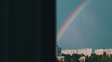 Bright rainbow in the sky over the city. Big colorful rainbow over houses. Strong rainbow above the city skyline over the houses and buildings in the daytime. The vivid phenomenon of nature. 4K