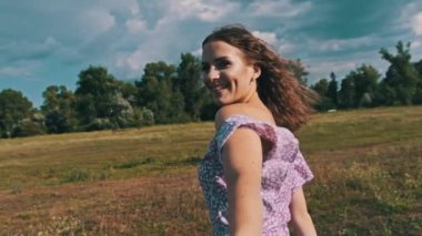 Genç ve çekici bir kadın erkek arkadaşını bir yaz otlağından çekiyor, beni takip edin, ağır çekim. Mutlu çiftin kırsal bir alanda el ele tutuşup doğanın tadını çıkardığı pov. Yaşam tarzı, aşk