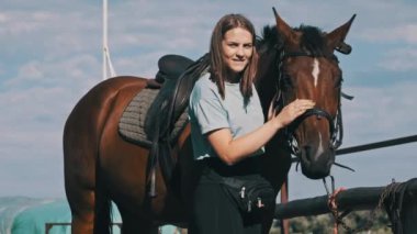 Happy woman stroking a horse on a farm in nature at summer day. Slow Motion. Beautiful girl pets brown horse near the stable. Friendship between human and animal. Mutual understanding, love for horses