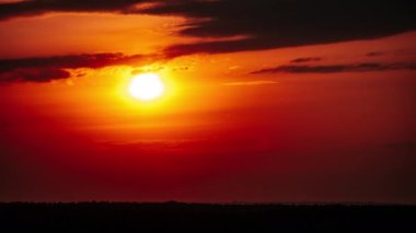 Timelapse of Dramatic sunset with sun rays in the sky through orange layered clouds. The big bright orange sun with sun rays moves down over the horizon. Awesome epic cloud space. Time Lapse. Sundown