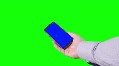 Male hand holding a smartphone with a blue screen and trackers on a green background. Chroma key. Alpha channel. Using the Device. Mobile Phone Screen. Replace blue screen and green screen. 4K