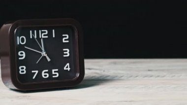 Tahta masa ve siyah arkaplan üzerindeki analog saat zamanı gösteriyor. İkinci el kare şeklindeki mekanik saatin kahverengi kadranı boyunca hareket eder. Zaman yönetimi, günlük rutin, iş, motivasyon