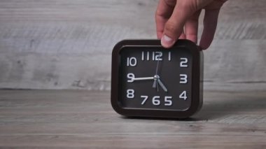 Erkek el, tahta masaya bir ok mekanik saati koyar. Kare şeklindeki işaretli kahverengi saat zamanı gösteriyor. İkinci el, yakın çekimde hareket eder. Kavram çizelgesi, erken kalkış, günlük rutin