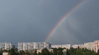 Bright rainbow in the sky over the city. Big colorful rainbow over houses. Strong rainbow above the city skyline over the houses and buildings in the daytime. The vivid phenomenon of nature. 4K