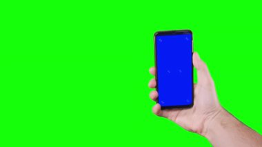 Male hand holding a smartphone with a blue screen and trackers on a green background. Chroma key. Alpha channel. Using the Device. Mobile Phone Screen. Replace blue screen and green screen. 4K