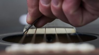 Yavaş çekimde akustik gitarda tellerin titreşimi. Klasik gitar metal telleri arabulucuya dokunurken titreşir. Slow Movement 240 fps, yakın çekim gitar destesi. Gitarist bronz tellere dokundu