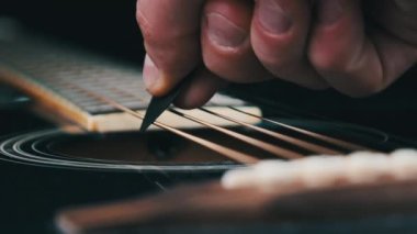 Yavaş çekimde akustik gitarda titreşimli metalik teller. Slow Movement 240 fps, yakın çekim gitar destesi. Klasik gitar telleri arabulucuya dokunurken titreşir. Gitarist bronz tellere dokundu