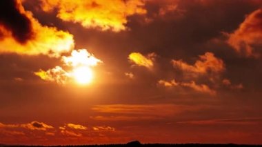 Dramatic sunset with sun rays in the Sky through orange layered clouds, Timelapse. The big bright orange sun with sun rays moves down over the horizon. Awesome epic cloud space. Time Lapse. Sundown