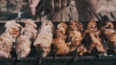 Grilling shashlik on barbecue grill outdoors. Process of cooking delicious shish kebab on a metal skewer in summer. Roast beef on BBQ. Marinated kebab grilled on charcoal. Weekend picnic. Street food