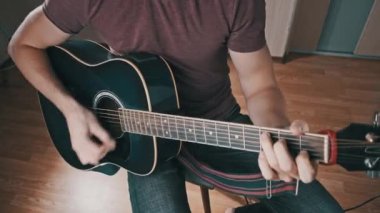 Gitarist evde akustik gitar çalar. Adam perdeleri tıngırdatır ve şarkıyı çalar. Klasik gitar çalmayı öğreniyorum. Genç müzisyen evdeki oturma odasında gitar çalıyor..