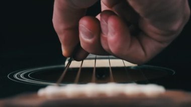 Yavaş çekimde akustik gitarda titreşimli metalik teller. Slow Movement 240 fps, yakın çekim gitar destesi. Klasik gitar telleri arabulucuya dokunurken titreşir. Gitarist bronz tellere dokundu