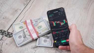 Tüccar, Ethereum 'un şifreli para birimini dolarlarla dolu bir masanın üstündeki akıllı telefon ekranında analiz ediyor. Bir telefon uygulamasında şifreleme ticareti. İş adamı dijital piyasayı inceliyor. Şifreli geleceğe yatırımlar