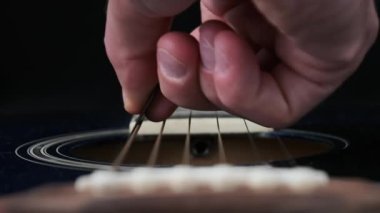 Yavaş çekimde akustik gitarda tellerin titreşimi. Klasik gitar metal telleri arabulucuya dokunurken titreşir. Slow Movement 240 fps, yakın çekim gitar destesi. Gitarist bronz tellere dokundu