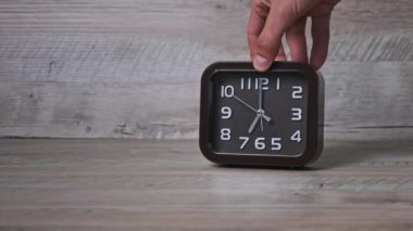 Erkek el, tahta masaya bir ok mekanik saati koyar. Kare şeklindeki işaretli kahverengi saat zamanı gösteriyor. İkinci el, yakın çekimde hareket eder. Kavram çizelgesi, erken kalkış, günlük rutin
