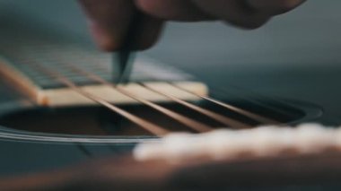 Yavaş çekimde akustik gitarda titreşimli metalik teller. Slow Movement 240 fps, yakın çekim gitar destesi. Klasik gitar telleri arabulucuya dokunurken titreşir. Gitarist bronz tellere dokundu