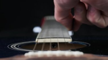 Yavaş çekimde akustik gitarda tellerin titreşimi. Klasik gitar metal telleri arabulucuya dokunurken titreşir. Slow Movement 240 fps, yakın çekim gitar destesi. Gitarist bronz tellere dokundu