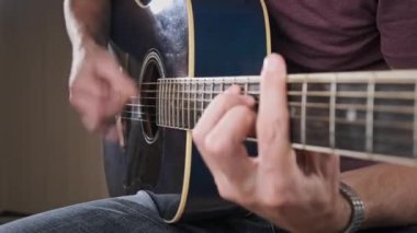 Gitarist evde akustik gitar çalar. Adam perdeleri tıngırdatır ve şarkıyı çalar. Klasik gitar çalmayı öğreniyorum. Genç müzisyen evdeki oturma odasında gitar çalıyor..