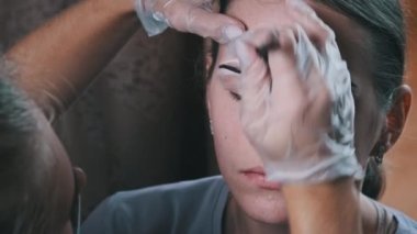 Eyebrow tinting procedure with henna in a beauty salon. The master brow corrects the shape of the eyebrows with a brush. A professional cosmetologist makes make-up. Face of a young girl close-up. 4K