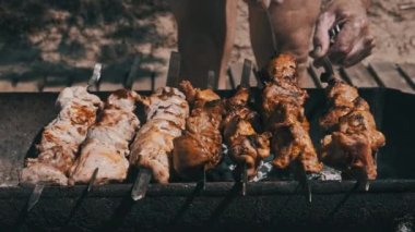Grilling shashlik on barbecue grill outdoors. Process of cooking delicious shish kebab on a metal skewer in summer. Roast beef on BBQ. Marinated kebab grilled on charcoal. Weekend picnic. Street food