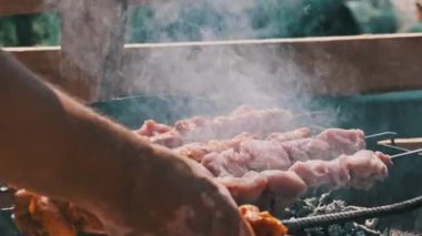 Grilling shashlik on barbecue grill outdoors. Process of cooking delicious shish kebab on a metal skewer in summer. Roast beef on BBQ. Marinated kebab grilled on charcoal. Weekend picnic. Street food