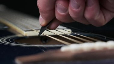 Yavaş çekimde akustik gitarda tellerin titreşimi. Klasik gitar metal telleri arabulucuya dokunurken titreşir. Slow Movement 240 fps, yakın çekim gitar destesi. Gitarist bronz tellere dokundu