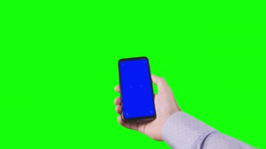 Male hand holding a smartphone with a blue screen and trackers on a green background. Chroma key. Alpha channel. Using the Device. Mobile Phone Screen. Replace blue screen and green screen. 4K