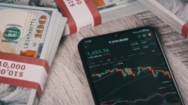 Ethereum kripto para birimi fiyatları bir akıllı telefon ekranında dolarlarla dolu bir masada. Dijital pazarın yanındaki bir telefon uygulamasında şifreli ticaret kavramı. Şifreli geleceğe yatırım. Kripto varlık fiyat tablosu