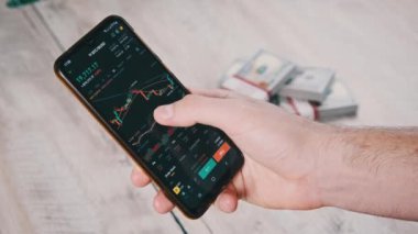 Şifreli akıllı telefon ticareti. İşadamı, dijital borsada dolarlarla dolu bir masanın üstündeki kripto fiyat tablosunu kontrol ediyor. BTC fiyatı. Kripto para ticareti. Çevrimiçi piyasa, değişim grafiği, Bitcoin