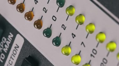 Vertical video LED indicator of sound level signal on mixing console. Close-up shot of strip in green and yellow on VU output level indicator. Volume level changes of indicator bulbs. Stereo meters