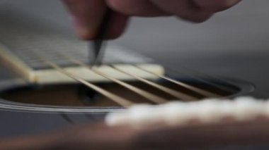 Yavaş çekimde akustik gitarda tellerin titreşimi. Klasik gitar metal telleri arabulucuya dokunurken titreşir. Slow Movement 240 fps, yakın çekim gitar destesi. Gitarist bronz tellere dokundu